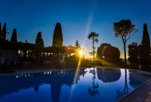 a swimming pool with the sun setting behind trees at Parco Fibonacci in Montefano