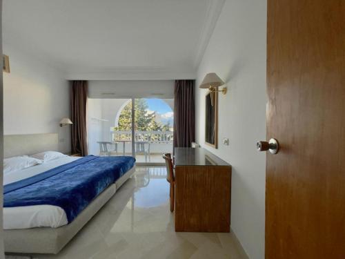 Residence Royal - Deluxe في Hammamet Sud: غرفة نوم بسرير ومكتب ونافذة