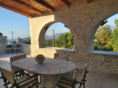 een stenen patio met een tafel en stoelen en 2 ramen bij Vasiliki Villa in Orthés