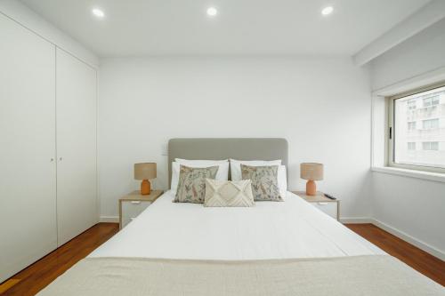 a white bedroom with a large white bed with two lamps at Modern Grand Seaside & Seaview by Vacationy in Matosinhos