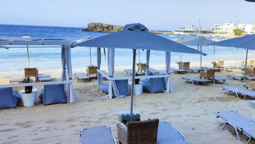 una playa con mesas azules, sillas y sombrillas en Le Grand Bleu Studios & Apartments, en Lefkos Karpathou
