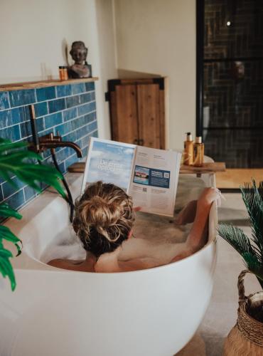 a man in a bath tub reading a magazine at Landgoed Lodges Scholten Linde in Rossum
