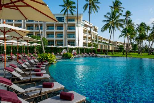 Phuket Panwa Beachfront Resort في شاطئ بنوا: فندق فيه مسبح والكراسي والمظلات