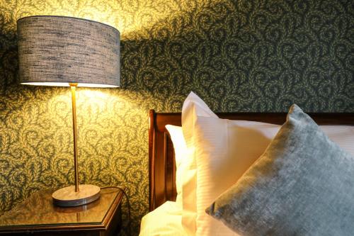 a lamp on a table next to a bed with pillows at The Black Swan in Ravenstonedale