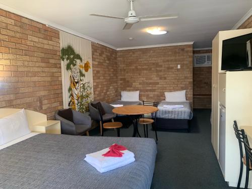 a room with two beds and a table and a tv at Shady Rest Motel in Gympie