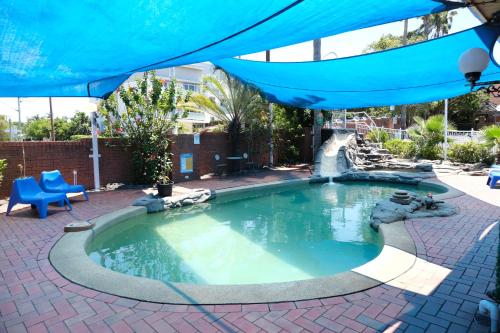 una piscina con cascada en un patio con sombrilla azul en Sapphire Palms Motel, en The Entrance