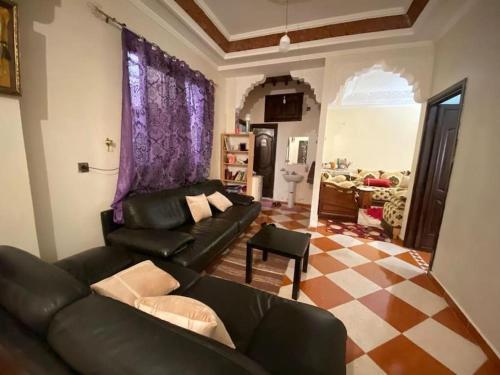 a living room with a black leather couch and a checkered floor at Grande maison Calme in Meknès