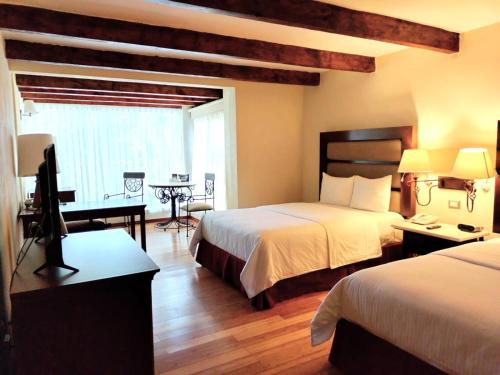 a hotel room with two beds and a desk at Hoteles Villa Mercedes San Cristobal in San Cristóbal de Las Casas
