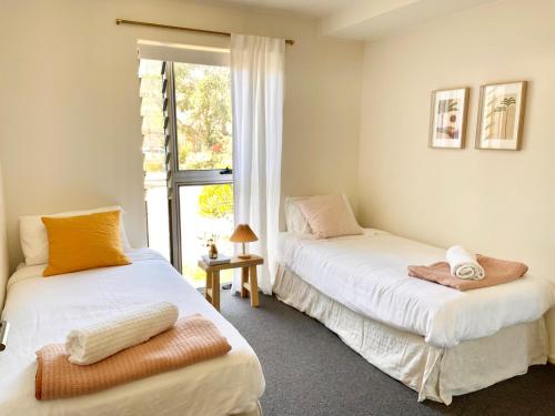 two beds in a room with a window at Cosy Apartment at Sebel Twin Waters Resort w Private Garden - 2 Mins Walk to Beach & River in Mudjimba