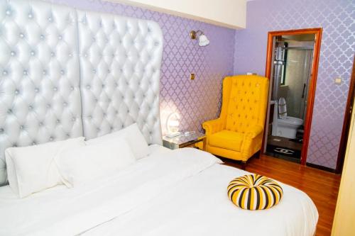 - une chambre avec un grand lit blanc et une chaise jaune dans l'établissement Lux Suites Marcus Garden Apartments kilimani, à Nairobi