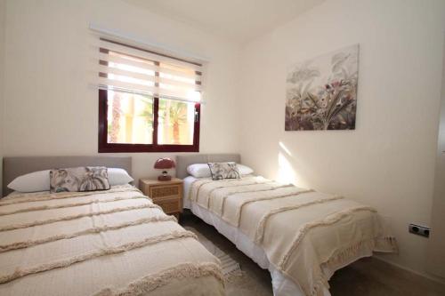 two beds in a white room with a window at Casa Hermana in Los Alcázares