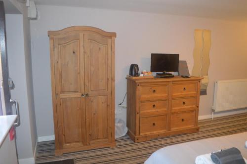 a bedroom with a wooden cabinet and a television on a dresser at The Queen Victoria in Snettisham