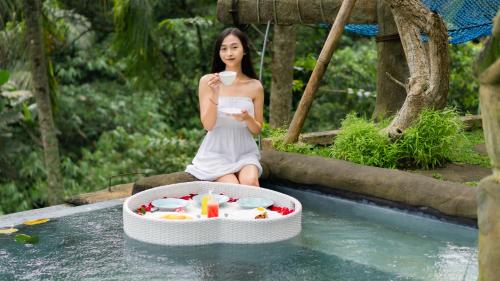 una donna seduta nell'acqua di una piscina con una vasca di cibo di Iyume Villas a Tegalalang