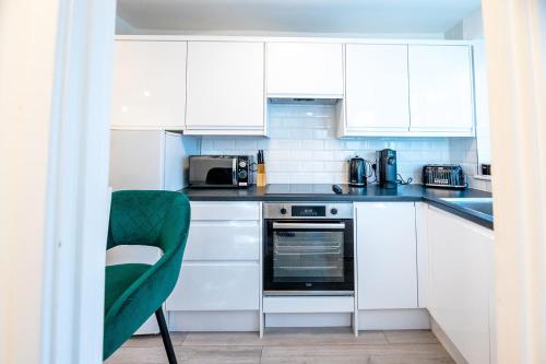 una cocina blanca con armarios blancos y una silla verde en Haygarth Apartment, en Knebworth