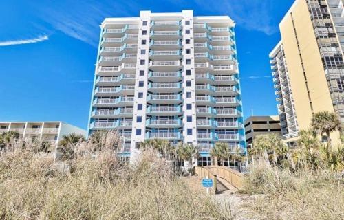 a tall white apartment building with trees in front of it at Ocean Blue - Ocean View Condos by Coastline Resorts in Myrtle Beach