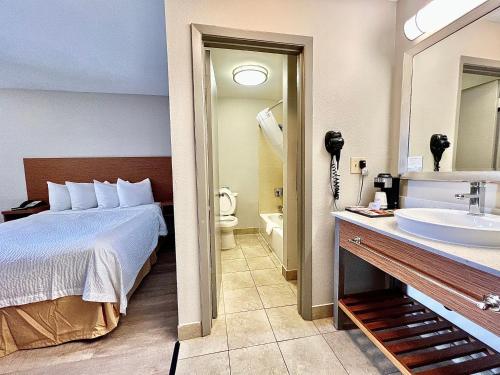 a hotel room with a bed and a bathroom with a sink at Days Inn & Suites by Wyndham Arlington Near Six Flags in Arlington