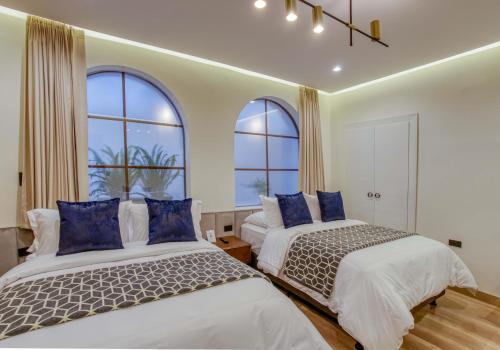 two beds in a room with two windows at Wanderlot - Hotel Plaza Central in Riobamba