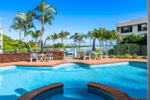 a swimming pool with chairs and palm trees at Little Cove Currumbin in Gold Coast