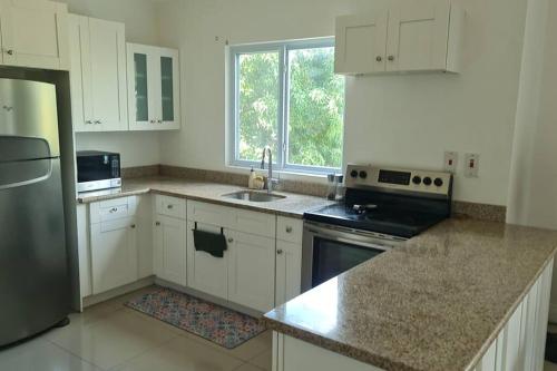 a kitchen with white cabinets and a sink and a refrigerator at Harloes Luxury Suite - Kingston Jamaica in Kingston