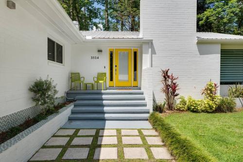 a white house with a yellow door and stairs at UF SUNSHINE HOUSE - Patio & BBQ & Fire Pit - Chef Kitchen - Upscale Neighborhood! in Gainesville