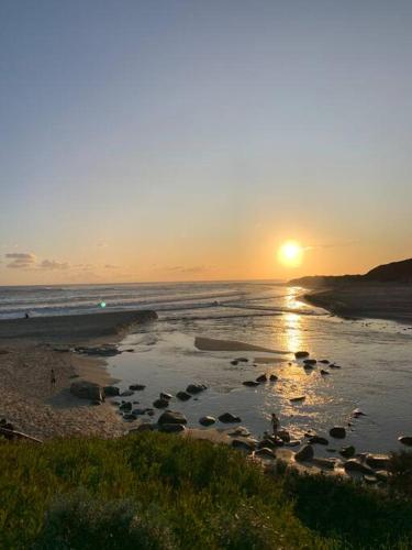 a sunset on a beach with the sun setting at Sleepy Hollow adorable peaceful guesthouse. in Gnarabup