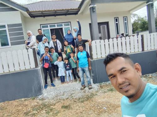 mężczyzna stojący przed rodziną przed domem w obiekcie Homestay Bendang Hilir w mieście Kuala Nerang