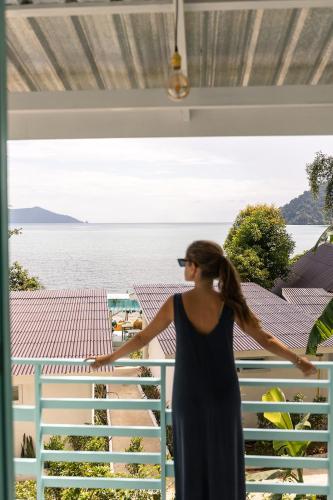 a woman standing on a balcony looking out at the water at Indie Beach Bungalows in Ko Chang