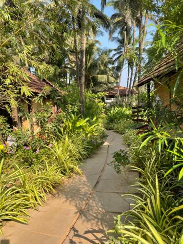 a path through a garden with palm trees and plants at The Village Anjuna in Anjuna