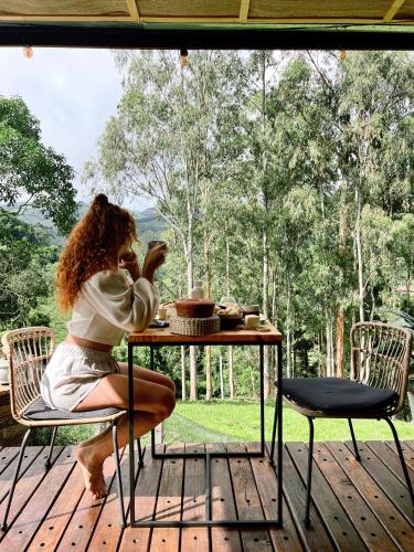 een vrouw aan een tafel op een dek bij LUTS Chalés in Gonçalves