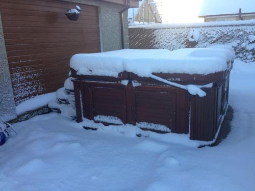 un cobertizo de madera cubierto de nieve con una puerta en un patio en Honeysuckle-Peaceful Scottish Cottage with Hot Tub en Airdrie