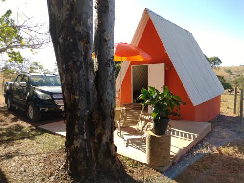 a small red house with a tree and a car at Camping e Pousada Buritis Park 