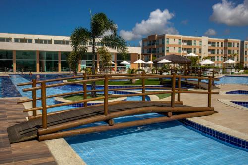 ein Resort-Swimmingpool mit Holzbänken und Sonnenschirmen in der Unterkunft Muro Alto Condomínio Club in Porto De Galinhas