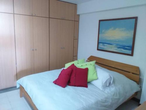 Un dormitorio con una cama blanca con almohadas rojas y verdes en Acogedor apartamento con piscina - Bleu Marine Suites, en La Guaira