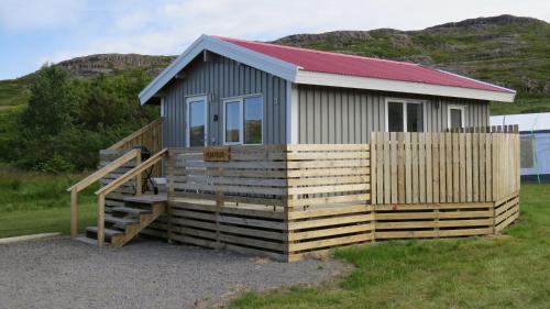 a small house with a wooden porch and a fence at Hvammur 3 Hrakhólar with private hot tub in Kaldrananes