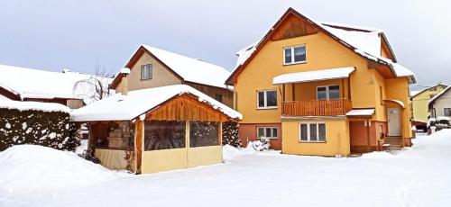 a yellow house with snow on the ground at Apartmány Grobarčík in Zuberec