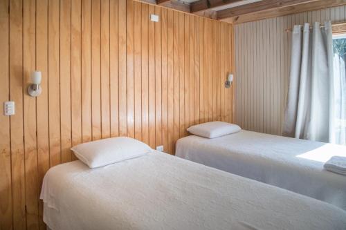 2 camas en una habitación con paredes de madera y ventana en La Casona, Baño Privado en Villa Cerro Castillo