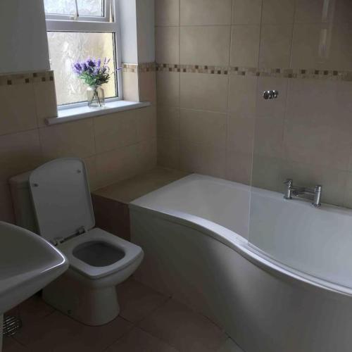 a bathroom with a tub and a toilet and a window at Harbour View House in Ballycastle