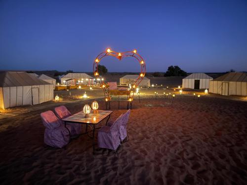 a table and chairs in the desert at night at Desert Sahara Luxury Camp in Merzouga