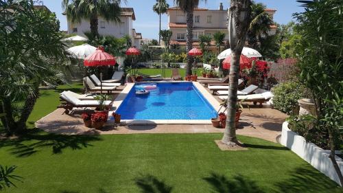 einen Pool mit Stühlen und Sonnenschirmen neben einem Gebäude in der Unterkunft Villa Sitges Palm Garden: 5 minutes walking from beach. Amaizing Garden/Outdoor in Sitges