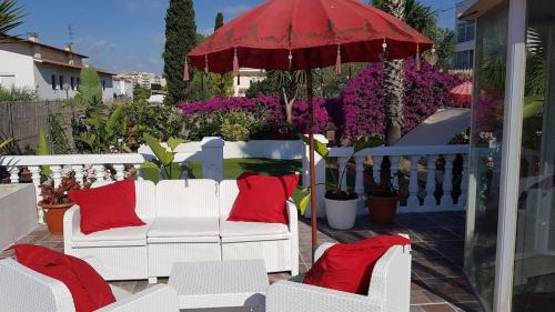eine Terrasse mit weißen Stühlen, roten Kissen und einem Sonnenschirm in der Unterkunft Villa Sitges Palm Garden: 5 minutes walking from beach. Amaizing Garden/Outdoor in Sitges