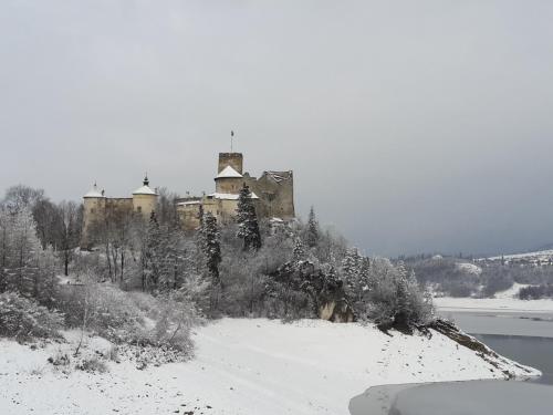 an old castle in the snow next to a body of water at Hotel**Pieniny in Niedzica