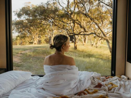 a woman sitting on a bed looking out a window at CABN Clare Valley in Mintaro