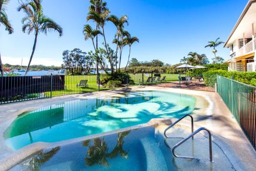 a swimming pool with blue water and palm trees at Cayman Quays in Noosaville