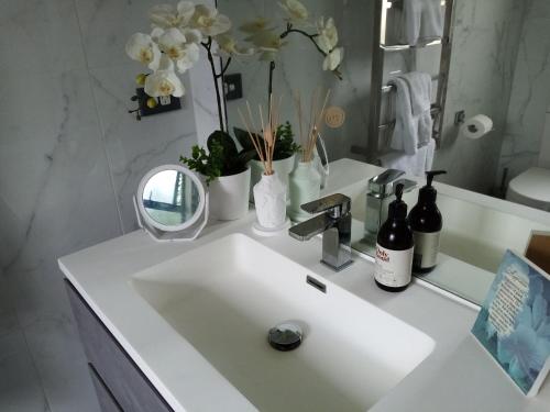 La salle de bains est pourvue d'un lavabo blanc, d'un miroir et de fleurs. dans l'établissement Sunbrae Beach Sanctuary free high Fibre wifi, à Mount Maunganui
