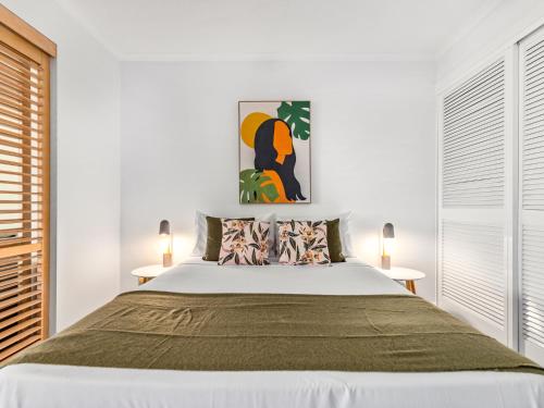 a white bedroom with a large bed and two tables at urban oasis in the heart of town in Port Douglas