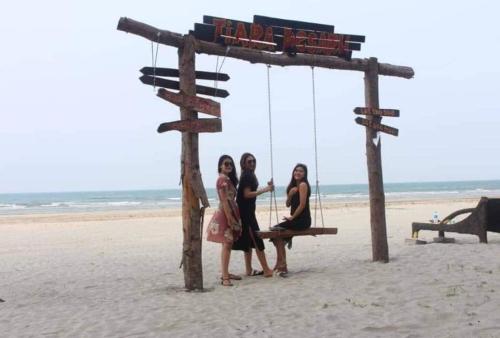 three women sitting on a swing on the beach at Balini Home Tiara Desaru in Desaru