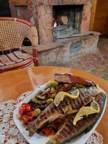 a plate of fish and vegetables on a table with a fireplace at Etno Guest House Gorski car in Arandjelovac