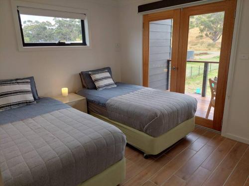 a bedroom with two beds and a door to a patio at The Beach Box at Big Roaring Beach Tasmania in Surveyors Bay