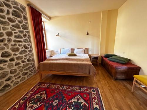 a bedroom with a bed and a couch and a stone wall at Saryan Guesthouse in Goris