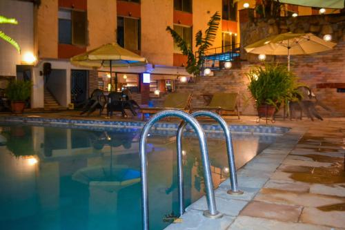 a swimming pool with chairs and umbrellas next to a building at Omega Gardens Hotel in Karatina